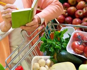 Woman checking shopping list with cart full of vegetables and fruit